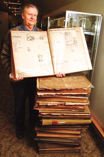 Jim West holds open a bound volume of the old Franklin Evening Star newspaper from 1942 while standing next to a stack of other volumes at the Camp Atterbury Museum.